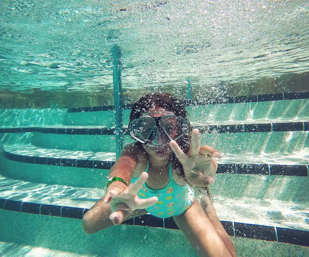 Young swimmer in goggles waving underwater