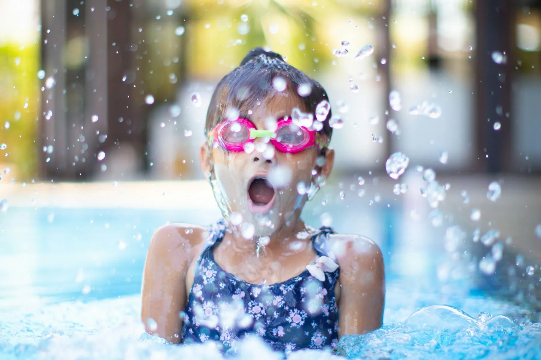 Young swimmer in pink goggles splashing happily in a pool