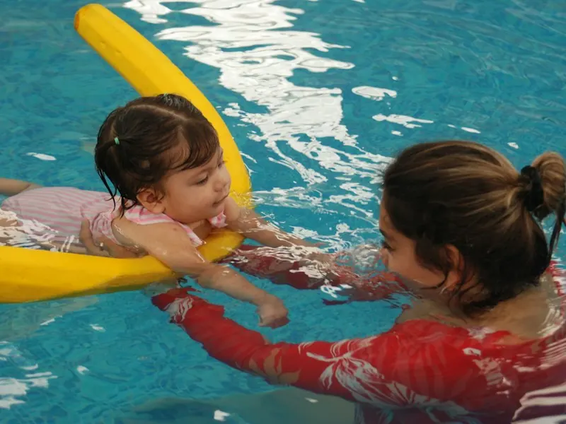 Swim instructor guiding a young child on a foam noodle