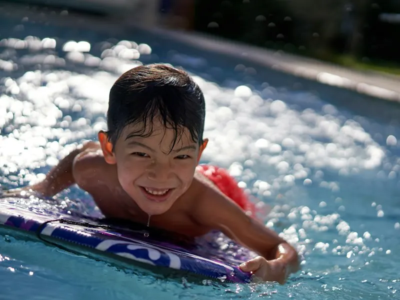 Smiling boy on a bodyboard in a backyard pool