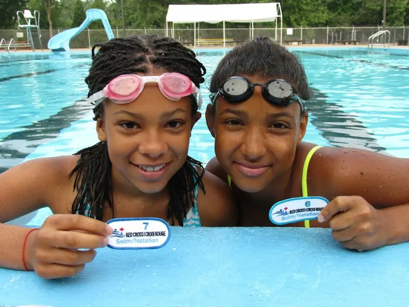 Two smiling young swimmers in goggles at the edge of a pool