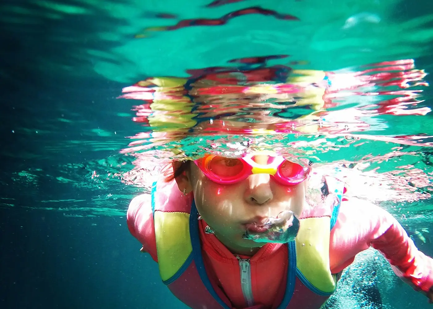 Child gliding underwater in pink goggles